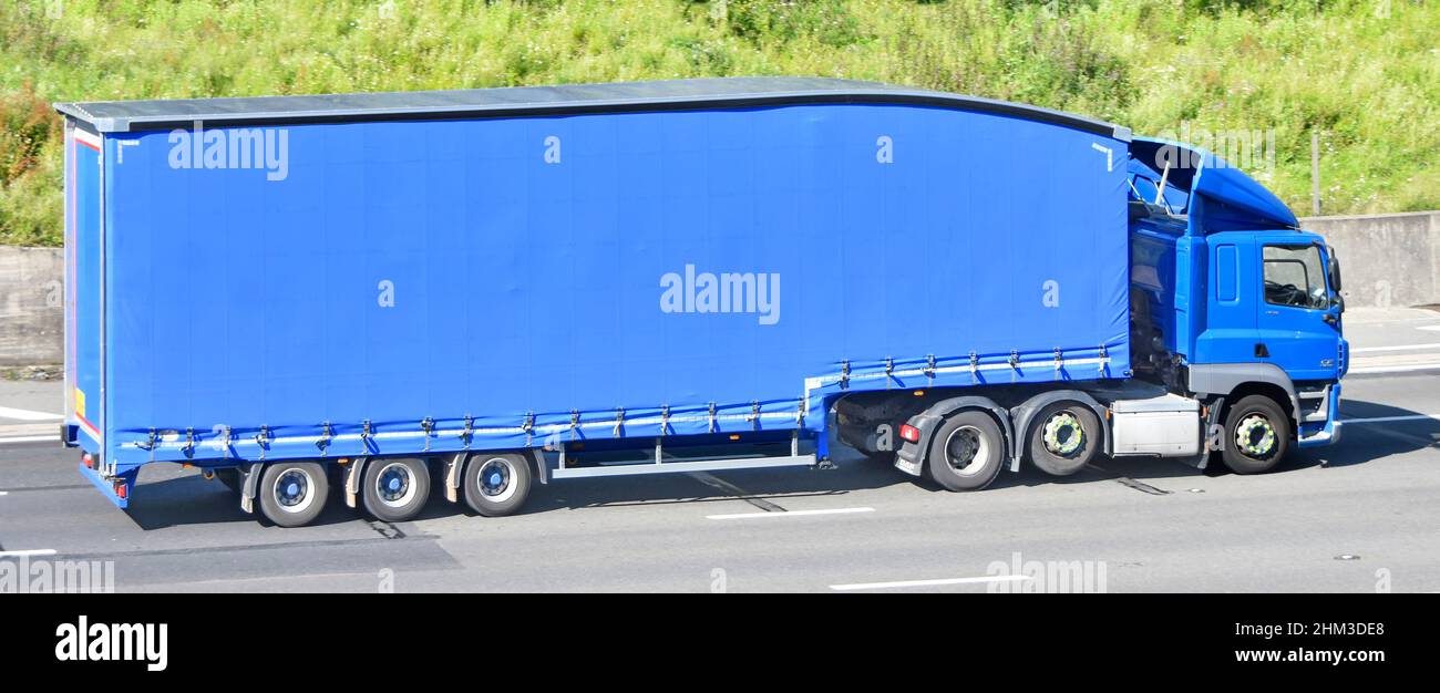 Blue hgv lorry truck & driver cab towing a clean streamlined unmarked articulated easy access curtain sider trailer driving motorway road England UK Stock Photo
