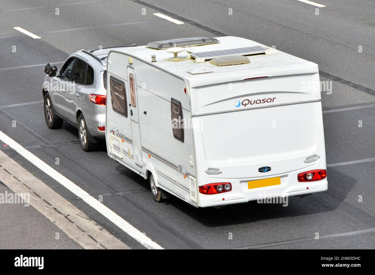 Holiday caravan Quosar brand aerial view roof mounted solar panel television aerial gas flue vent & rooflight side view car towing on UK motorway road Stock Photo