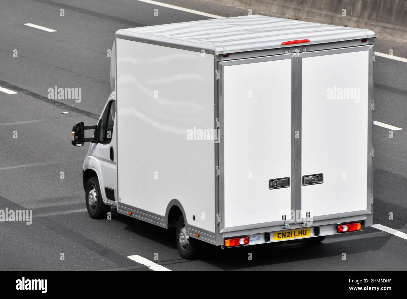 Back side & aerial view of square shape all white clean box van with back doors built onto a white standard chassis cab vehicle on UK motorway road Stock Photo