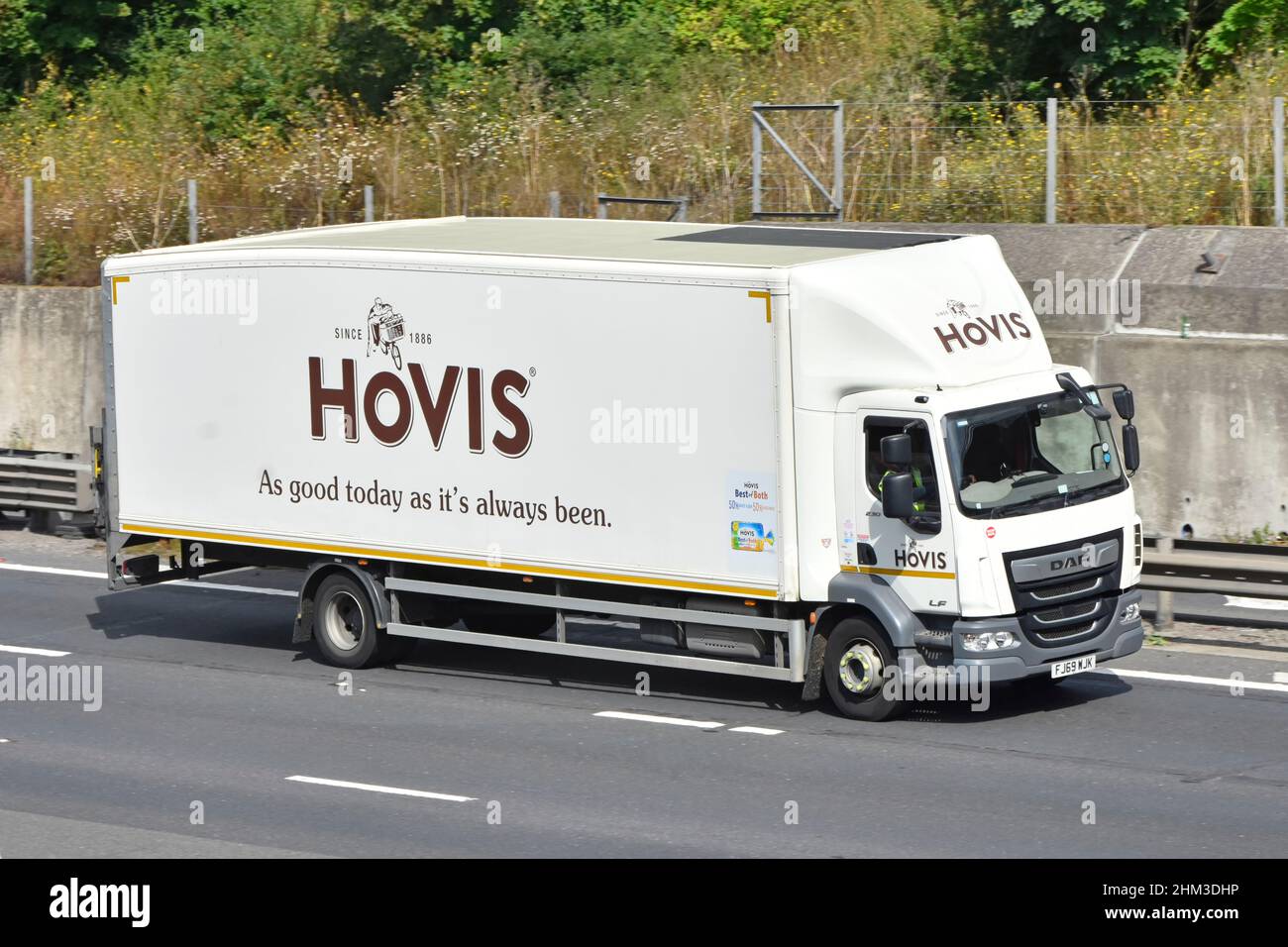Hovis business brand logo side & front view white rigid body food supply chain transport delivery lorry truck & driver driving along uk motorway road Stock Photo