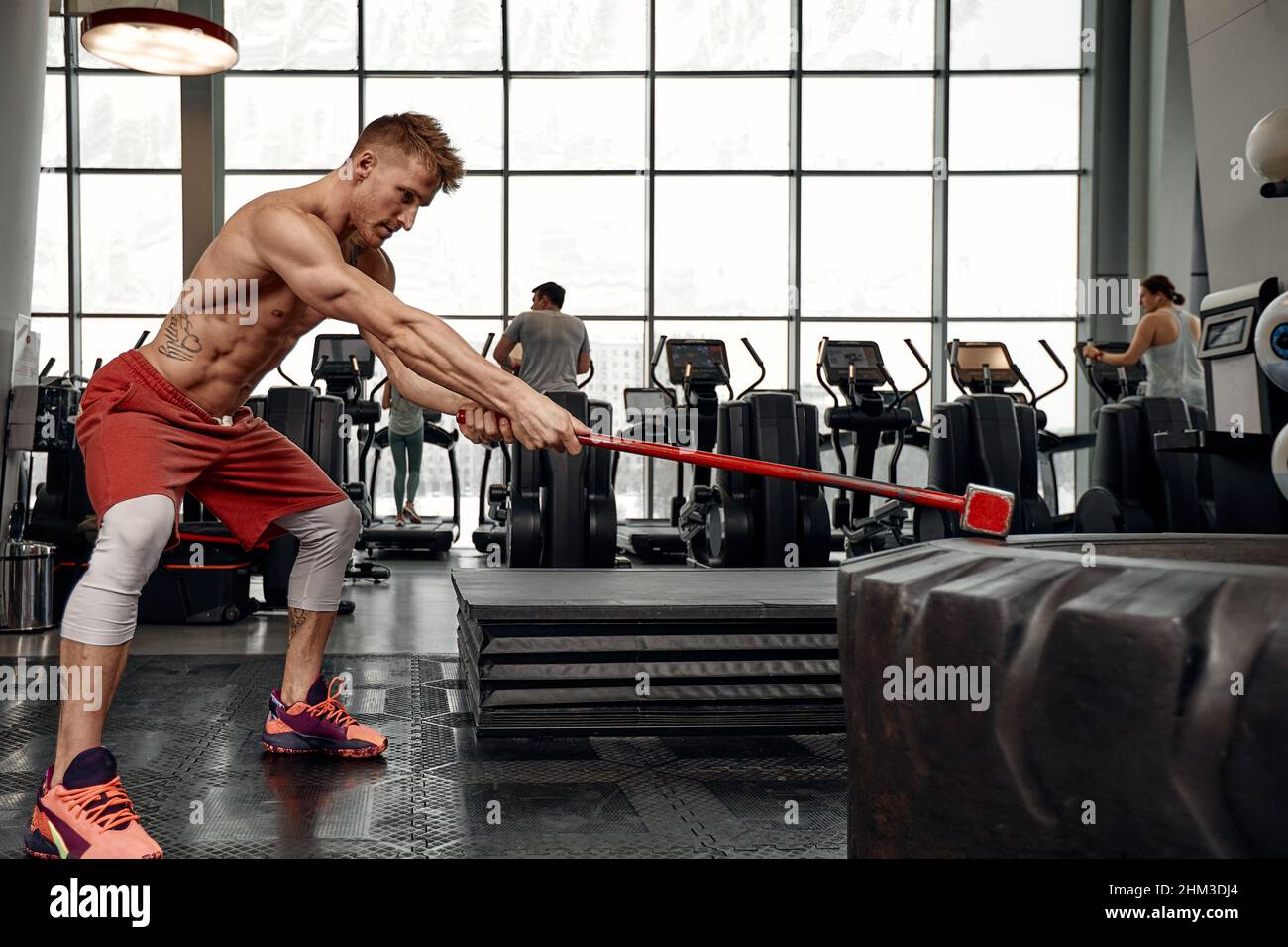 Strength concept. Male athlete using hammer during fitness workout. Fitness  man beating rubber tire in gym. Muscular sportsman performing intensity tr  Stock Photo - Alamy
