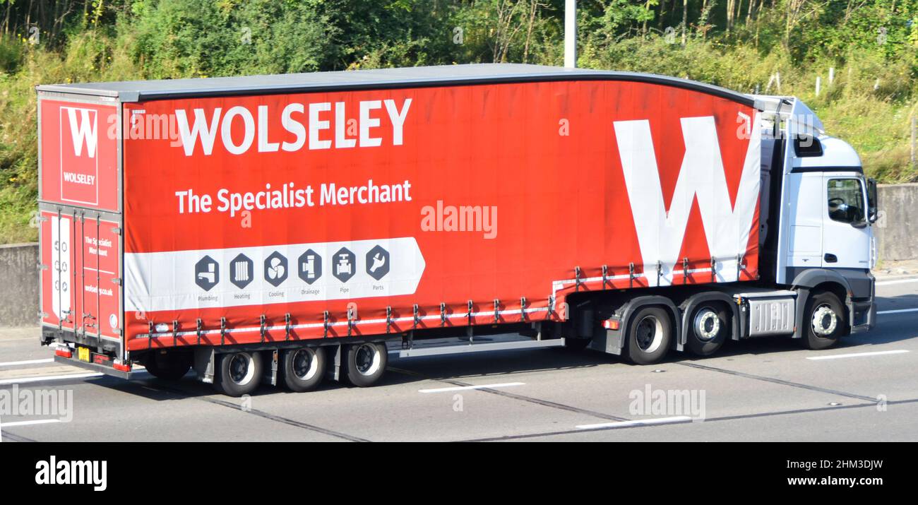 Wolseley plumbing heating specialist merchant business red articulated trailer with logo towed by white Daff hgv lorry truck driving along UK motorway Stock Photo