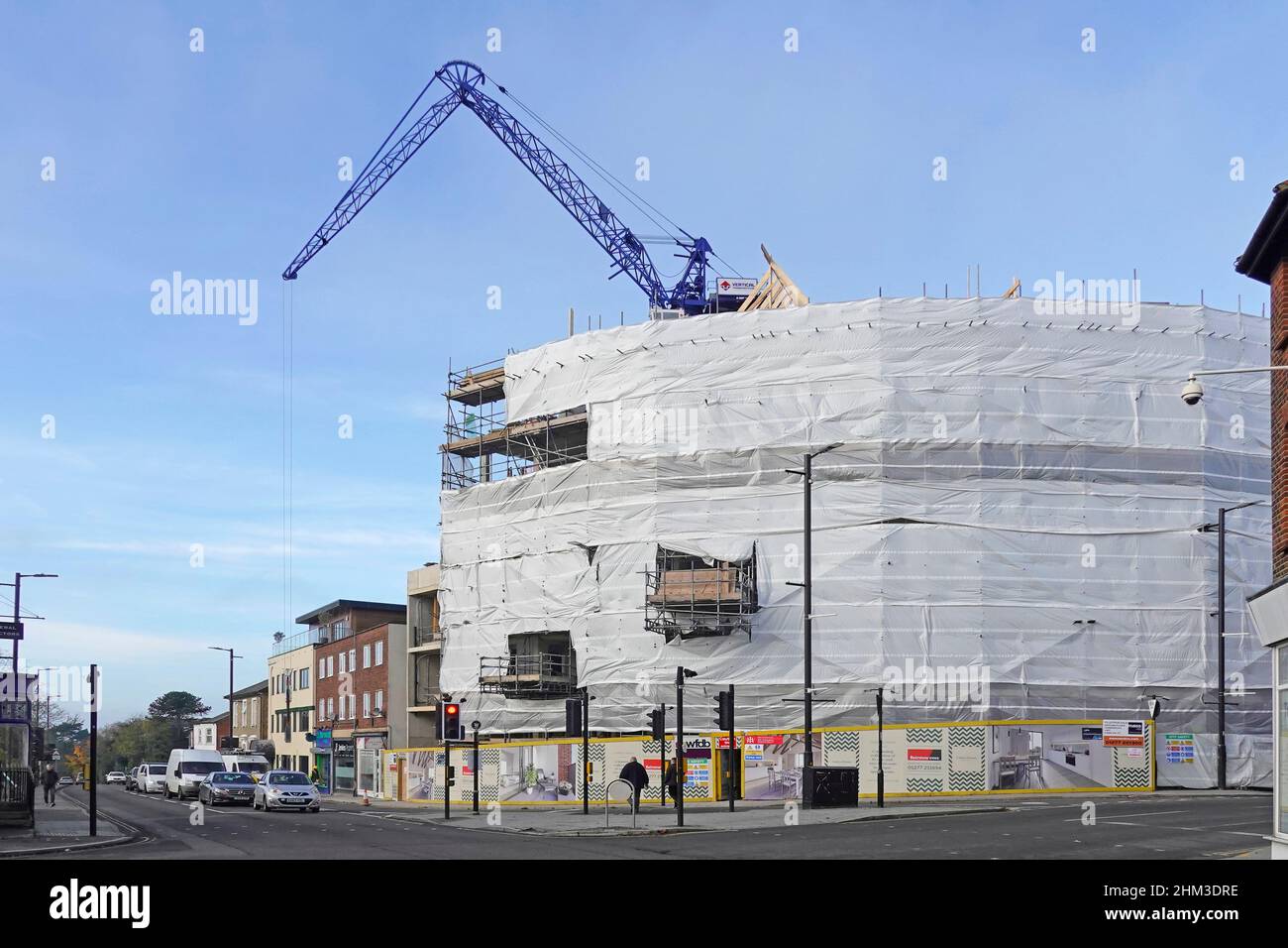 Construction site crane on prime corner plot at busy high street road junction plastic safety cocoon around scaffolding & building work Brentwood UK Stock Photo