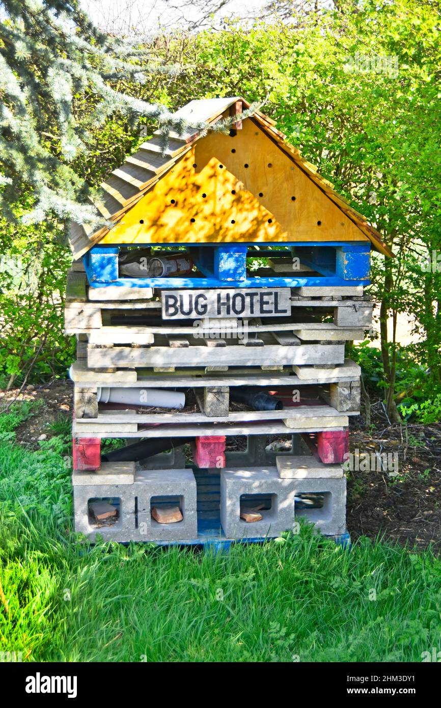 Close up man made Bug Hotel insect house in shady corner of gardeners patch in churchyard cemetery made of timber pallets & concrete blocks England UK Stock Photo