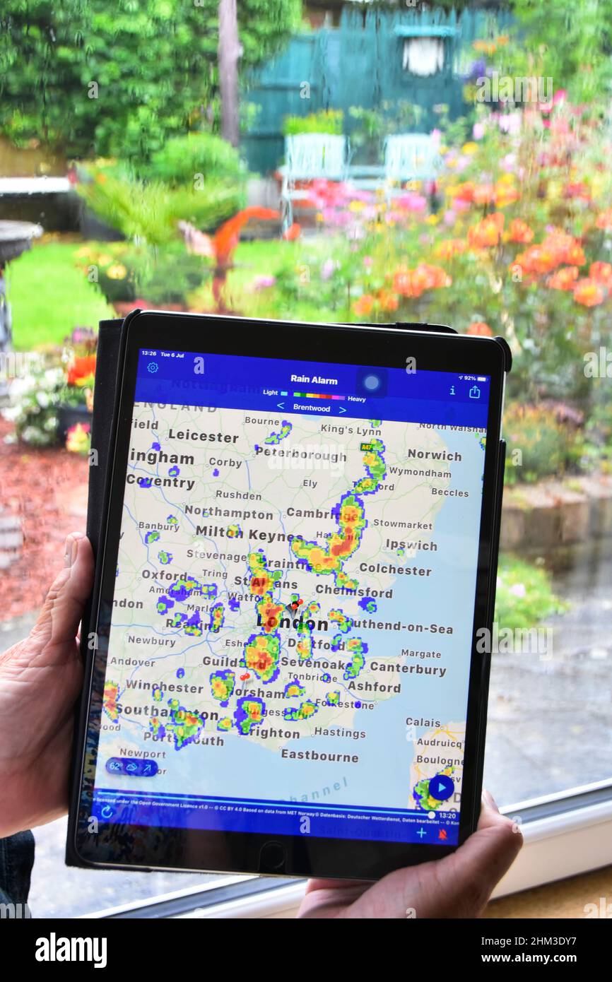 Real time colour radar ipad app data shows rainfall on local map woman waits for wet weather to clear on home window get back to gardening Essex UK Stock Photo