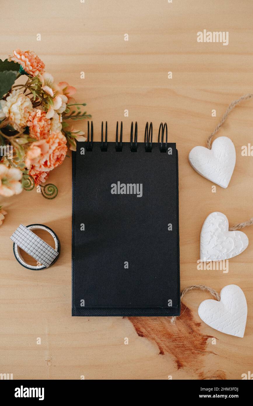 notebook with black sheets with copy space, on a wooden table with a bouquet of flowers and a white heart. Stock Photo