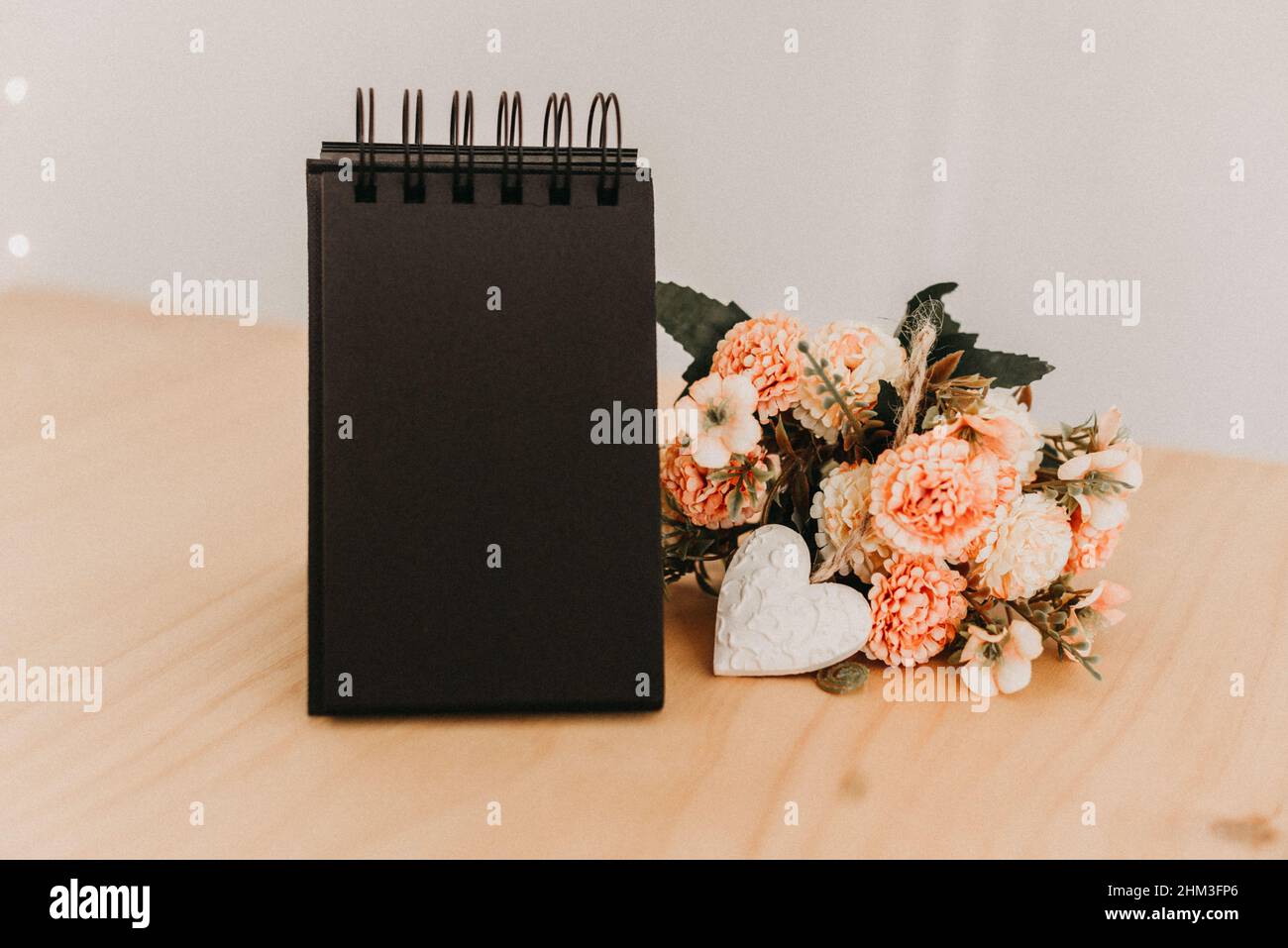 notebook with black sheets with copy space, on a wooden table with a bouquet of flowers and a white heart. Stock Photo