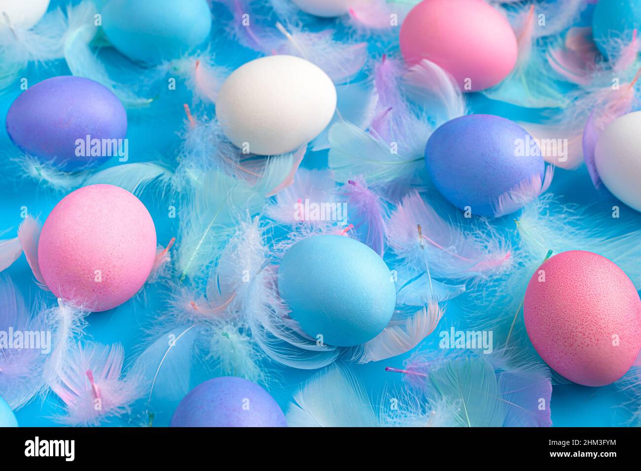 Easter background with colored eggs and feathers on a blue background. Side view, close-up. Stock Photo