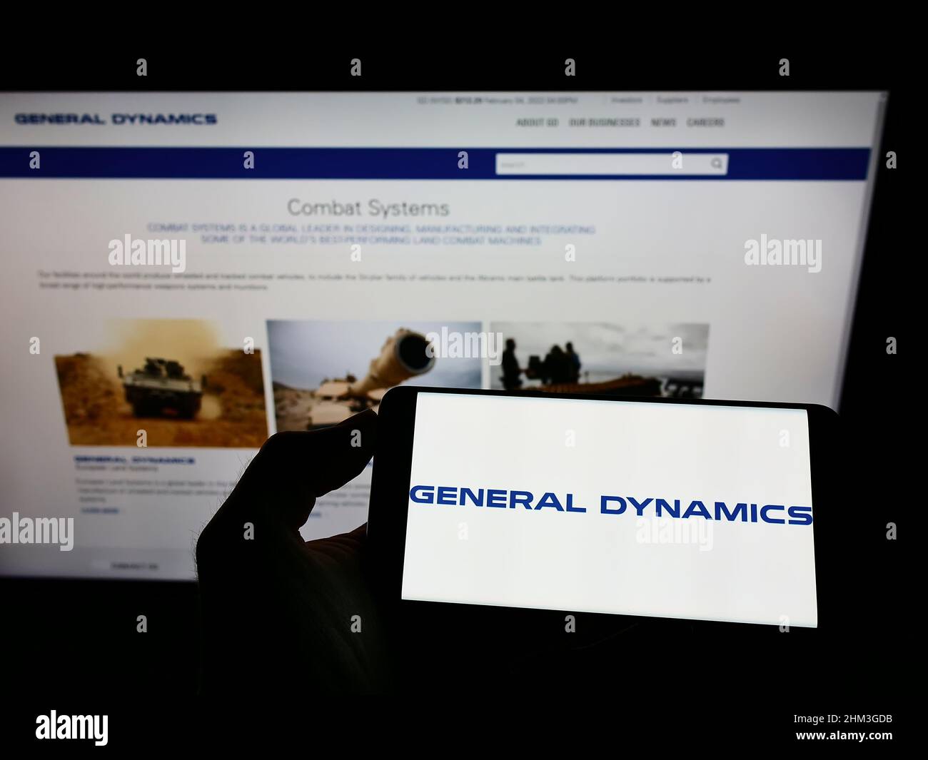 Person holding cellphone with logo of American company General Dynamics Corporation (GD) on screen in front of webpage. Focus on phone display. Stock Photo