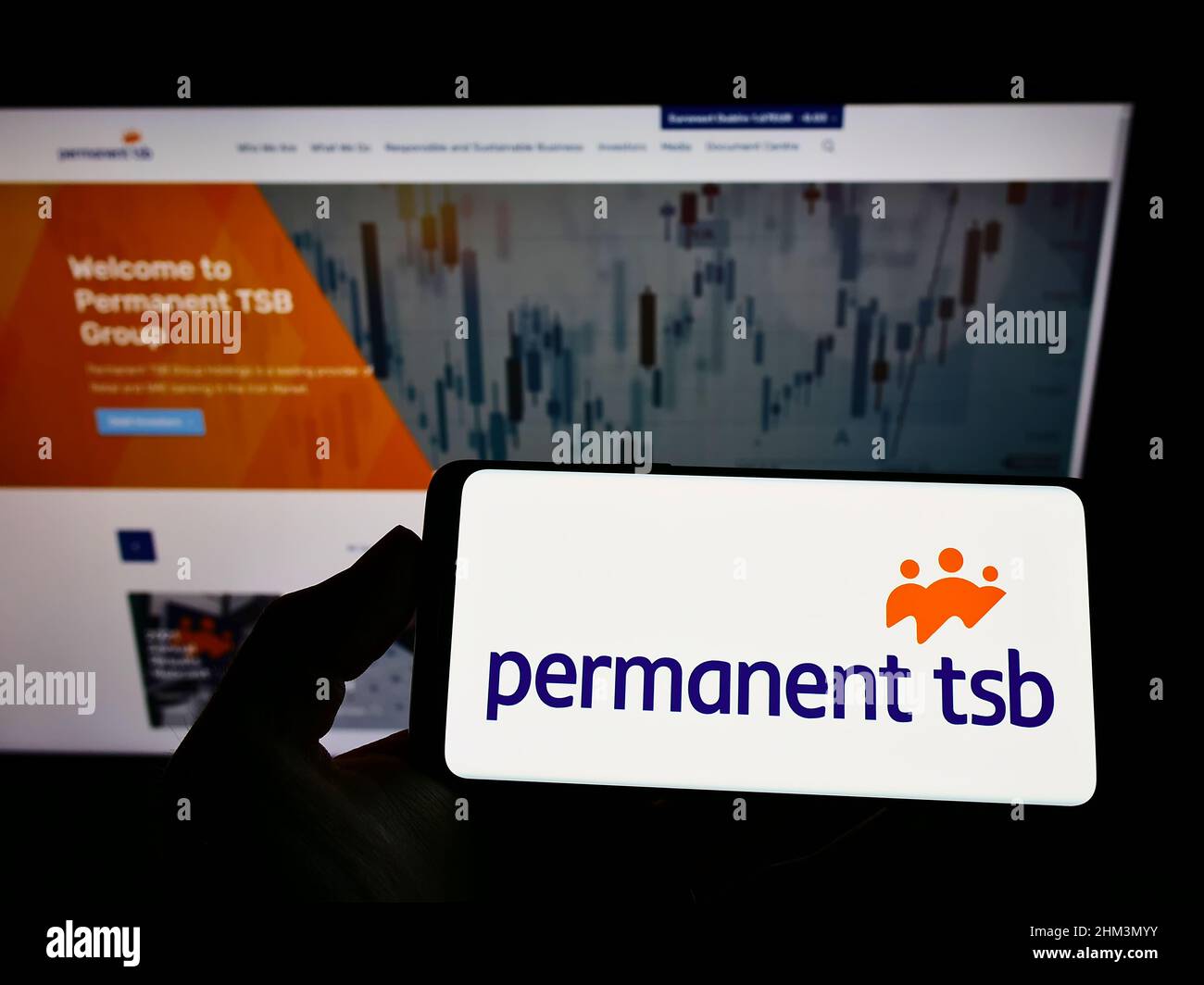 Person holding smartphone with logo of Irish company Permanent TSB Group Holdings plc on screen in front of website. Focus on phone display. Stock Photo