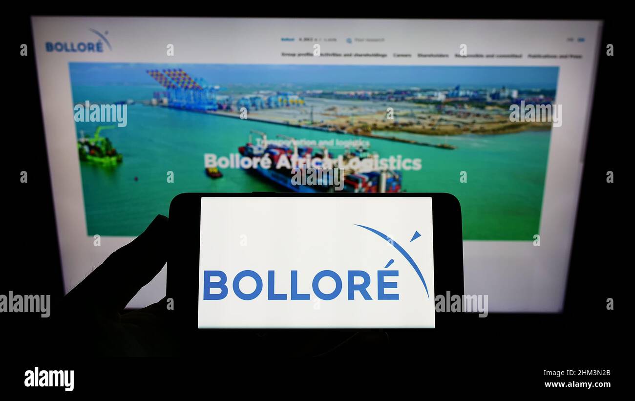Person holding smartphone with logo of French conglomerate company Bollore SE on screen in front of website. Focus on phone display. Stock Photo