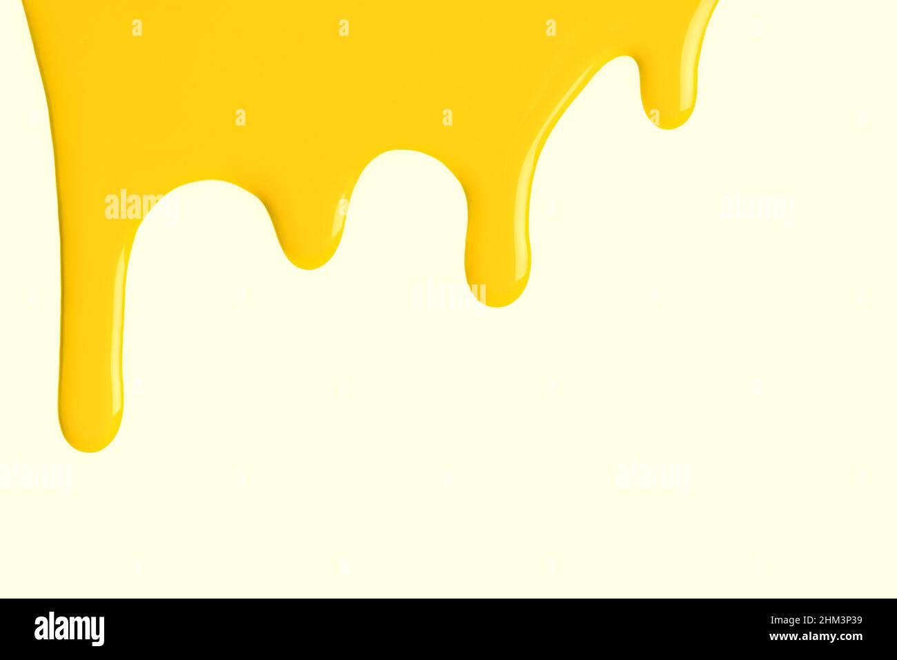 Bright yellow liquid drops of paint color flow down on isolated cream