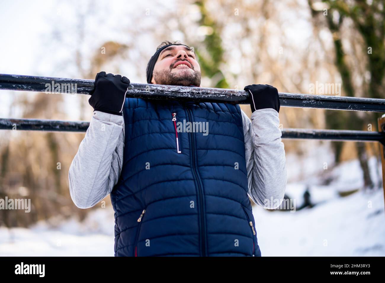 Adult man is exercising on pull-up bar in park in wintertime. Stock Photo