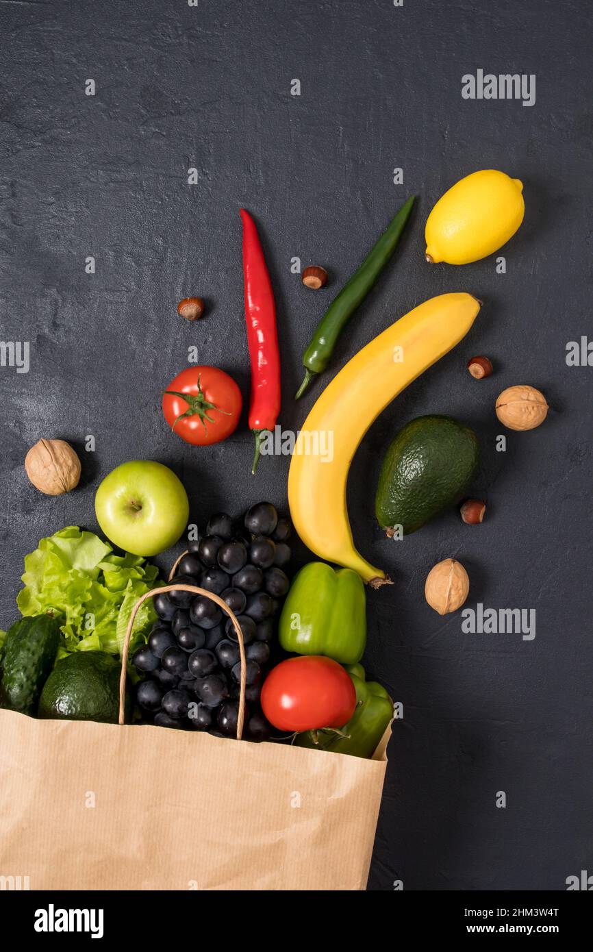 Kraft paper bag filled with fresh vegetables and fruits on a black ...
