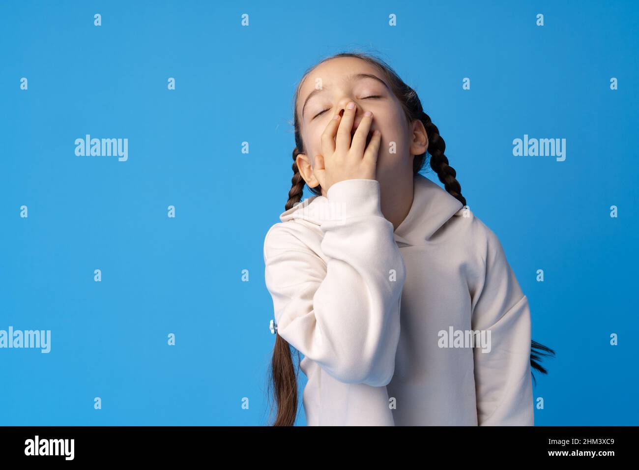 A tired little girl yawning on blue background. Stock Photo
