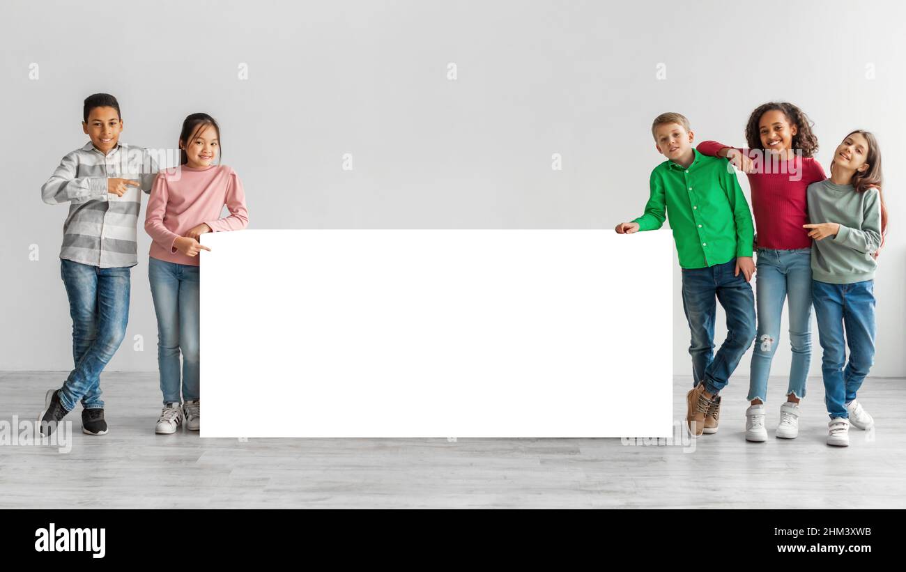 Happy Diverse Kids Standing Near White Board Over Gray Background Stock Photo