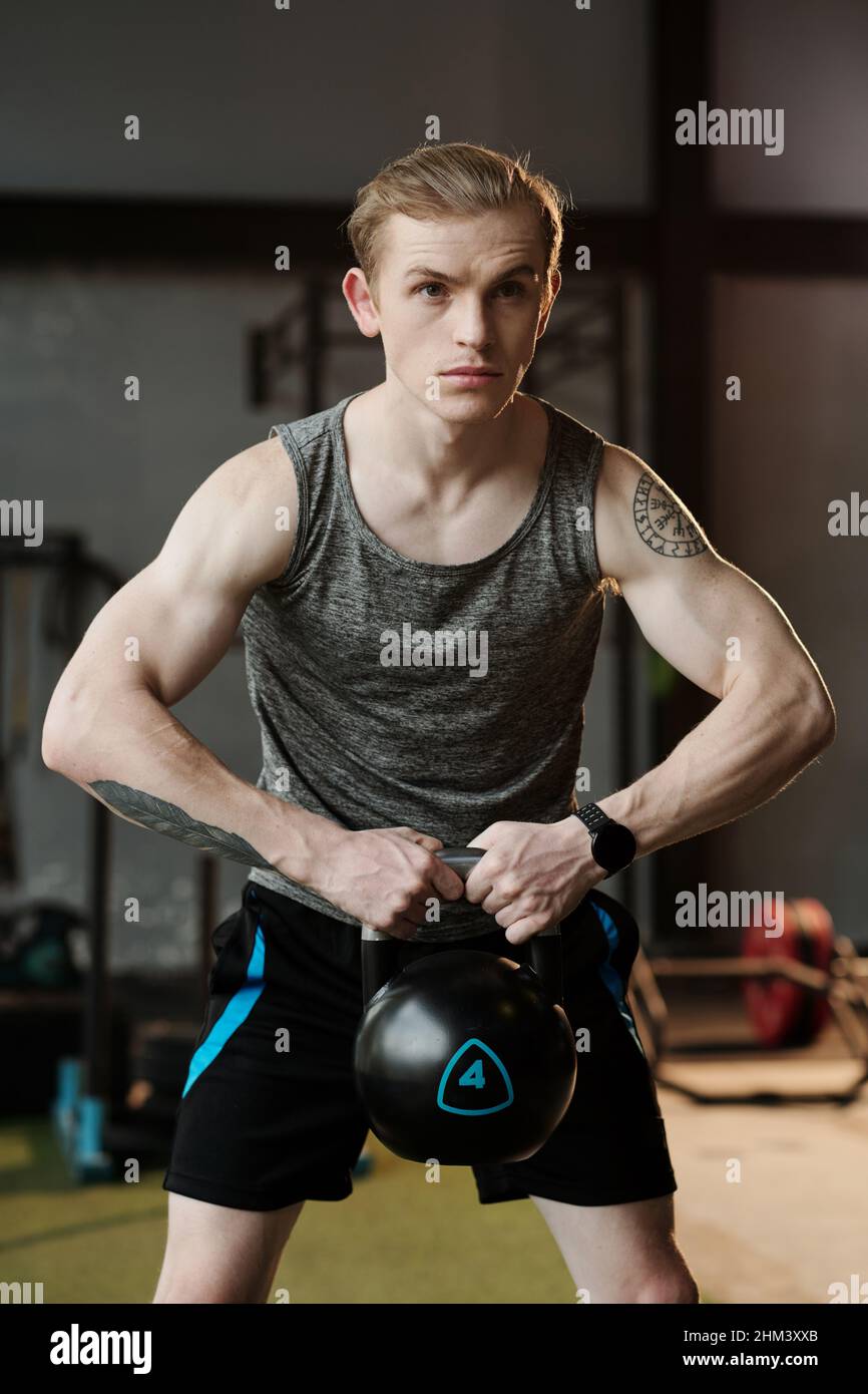 Muscular young man lifting heavy kettle bell when working out in gym Stock Photo