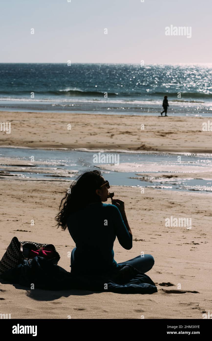 Carcavelos Beach, Portugal - February 5, 2022: Young woman enjoys an ice cream on a sunny winter day at Carcavelos beach in Lisbon Region, Portugal Stock Photo
