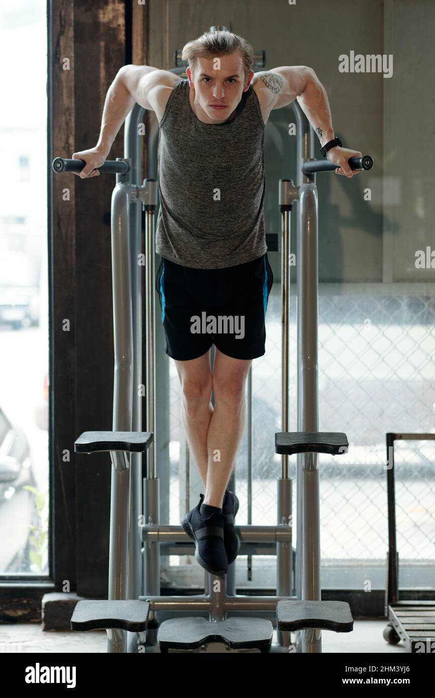 Fit young man doing exercise on pull-up machine when working out of triceps Stock Photo