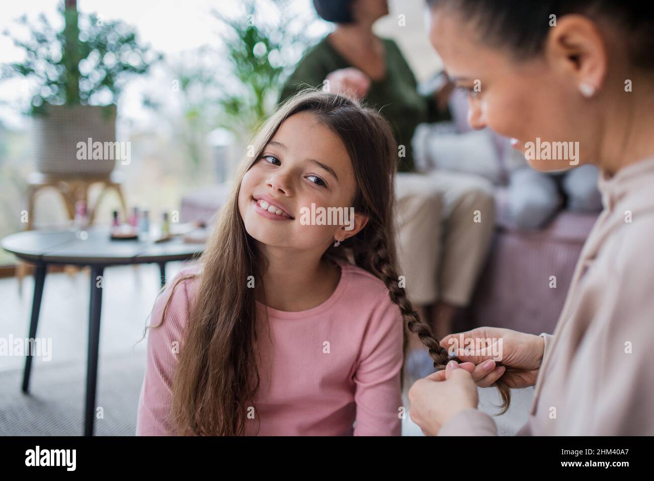 Mother making a plait to little daughter at home. Stock Photo
