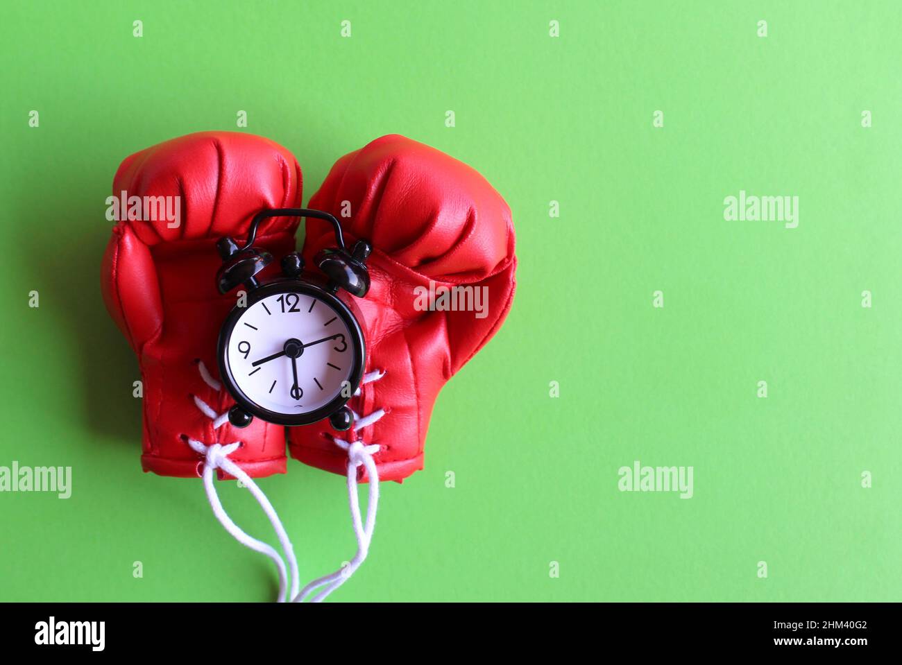 Training and exercise time. Top view image of boxing gloves and alarm clock on green background. Stock Photo