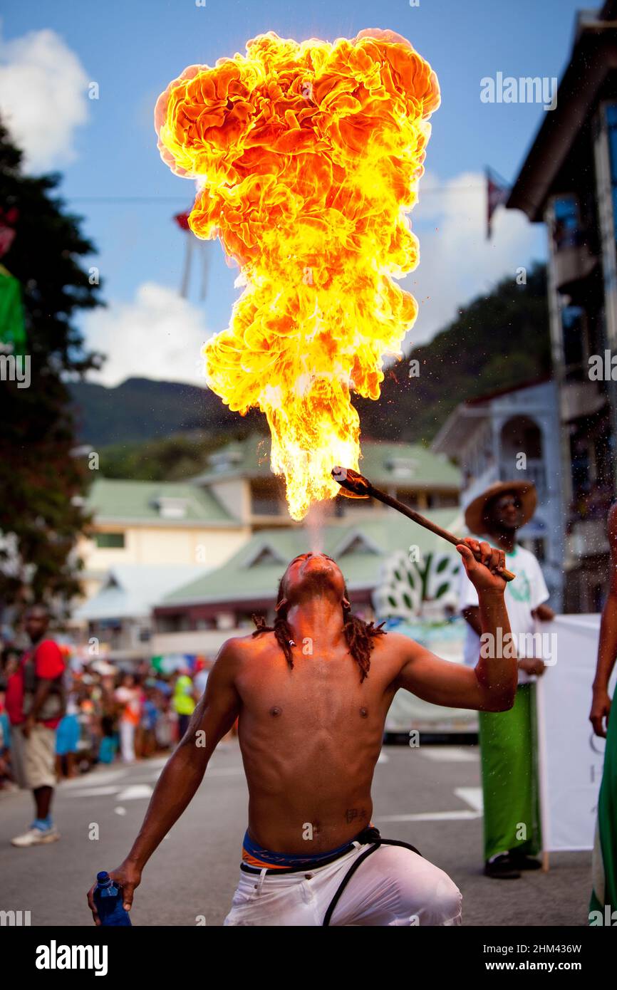 A shirtless fire breather blows a powerful plume of flames into the air during Seychelles international carnival. Stock Photo
