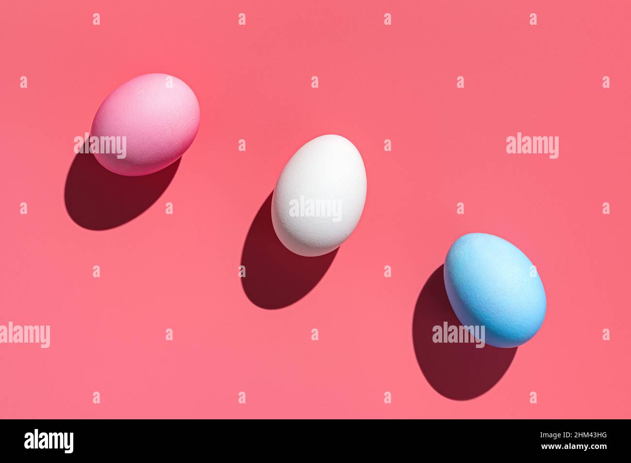 Three Easter eggs of different colors on a pink background. Abstract Easter background. Stock Photo