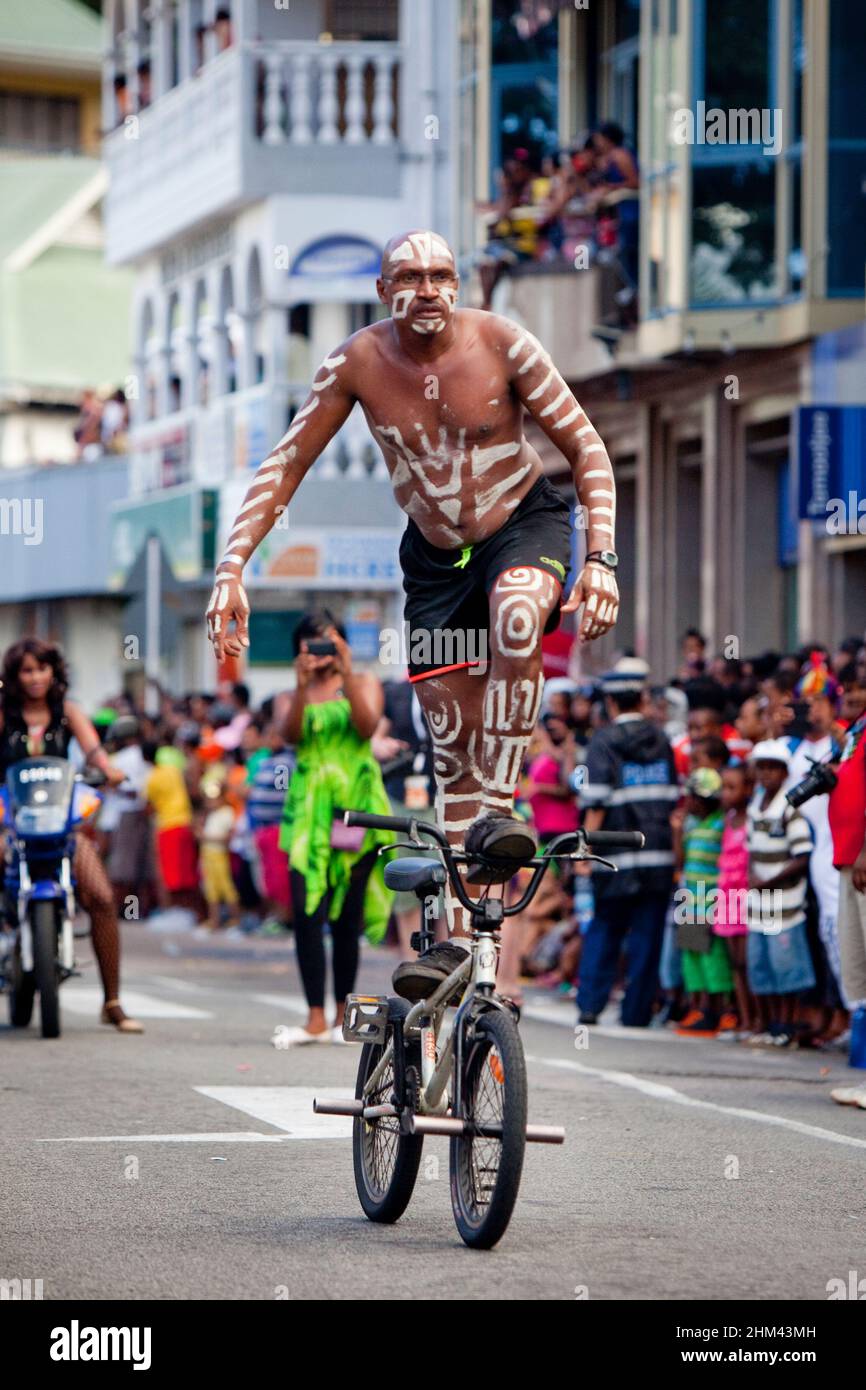 Shirtless man in body paint performs BMX tricks for the crowd in the street during Seychelles international carnival. Stock Photo