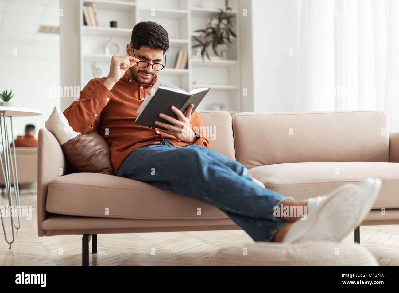 Focused Arab man in glasses trying to read book Stock Photo