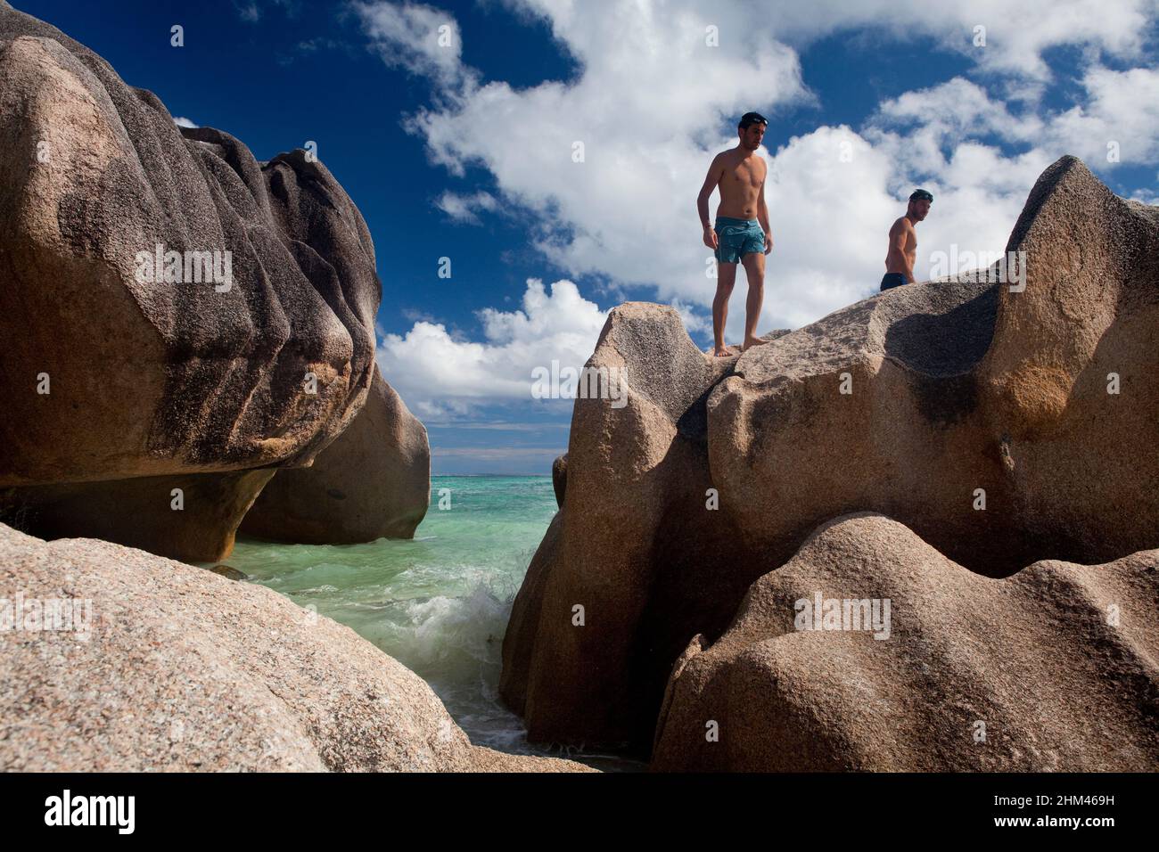 A couple of tourists boulder hopping at Grand Anse Beach, La Digue Island, Seychelles. Stock Photo