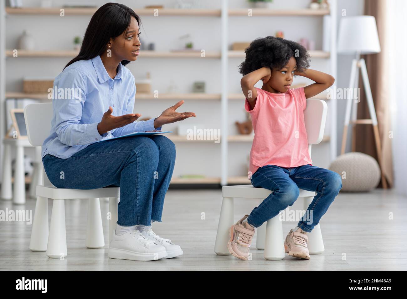 African american woman psychotherapist talking to unruly little girl Stock Photo