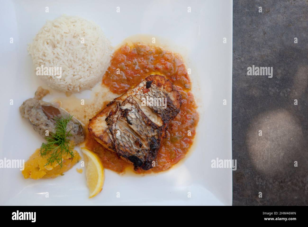 Grilled fish, rice, sauces and lemon on a dinner plate. Stock Photo