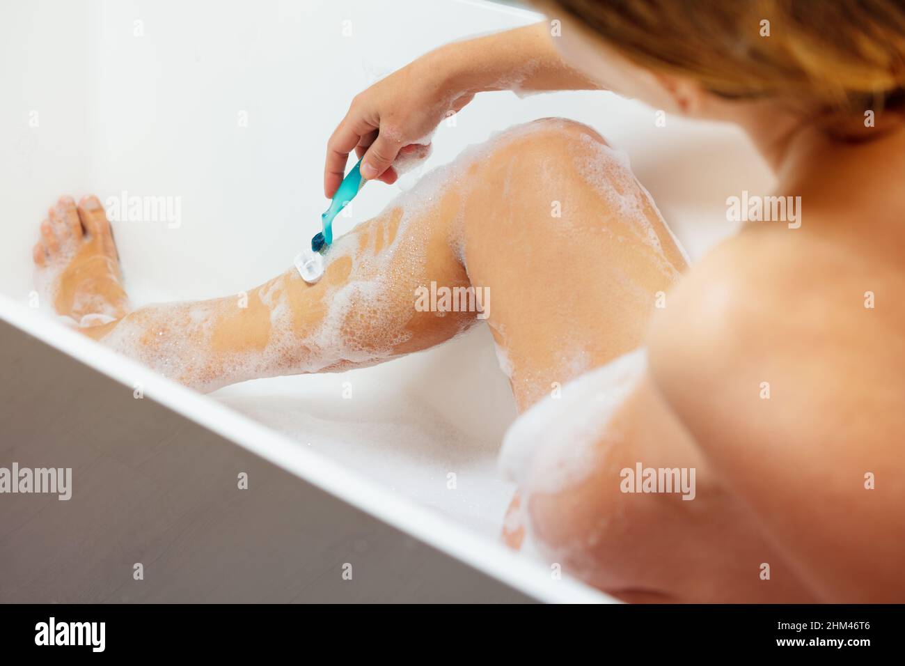 Woman shave leg sitting in bath with foam Stock Photo