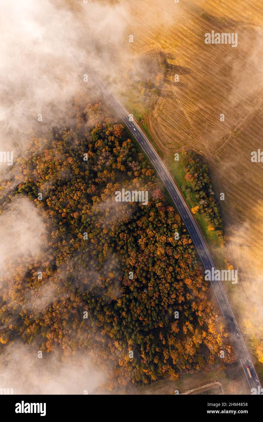Aerial view on a rural highway during fall season. Autumn bright foliage and cars moving through clouds of fog Stock Photo