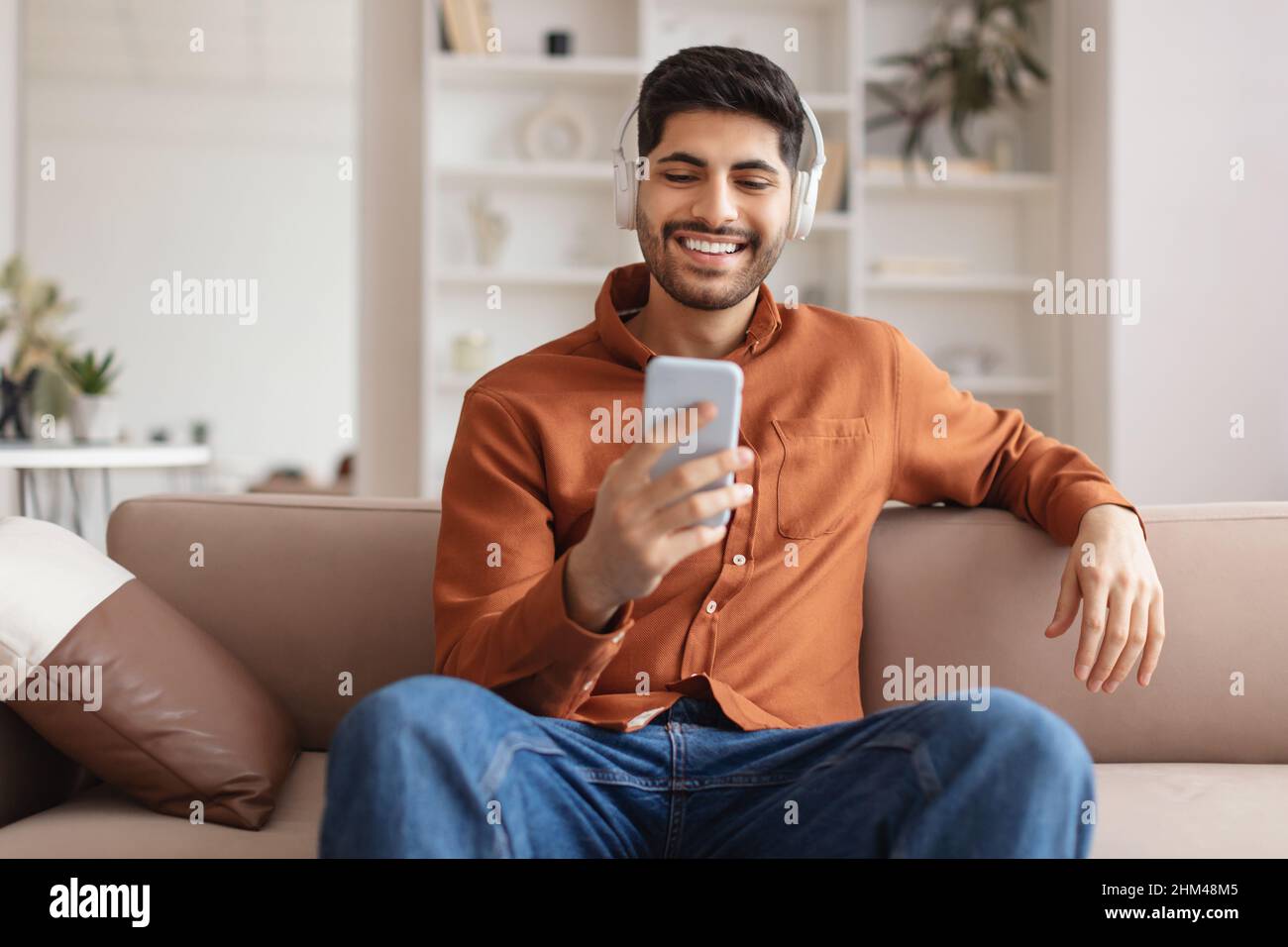 Smiling bearded man in wireless headhones using cellphone Stock Photo