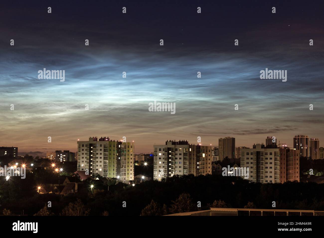 City buildings against a background of beautiful luminous silvery mesospheric clouds. Atmospheric phenomenon glowing of noctilucent clouds in the nigh Stock Photo