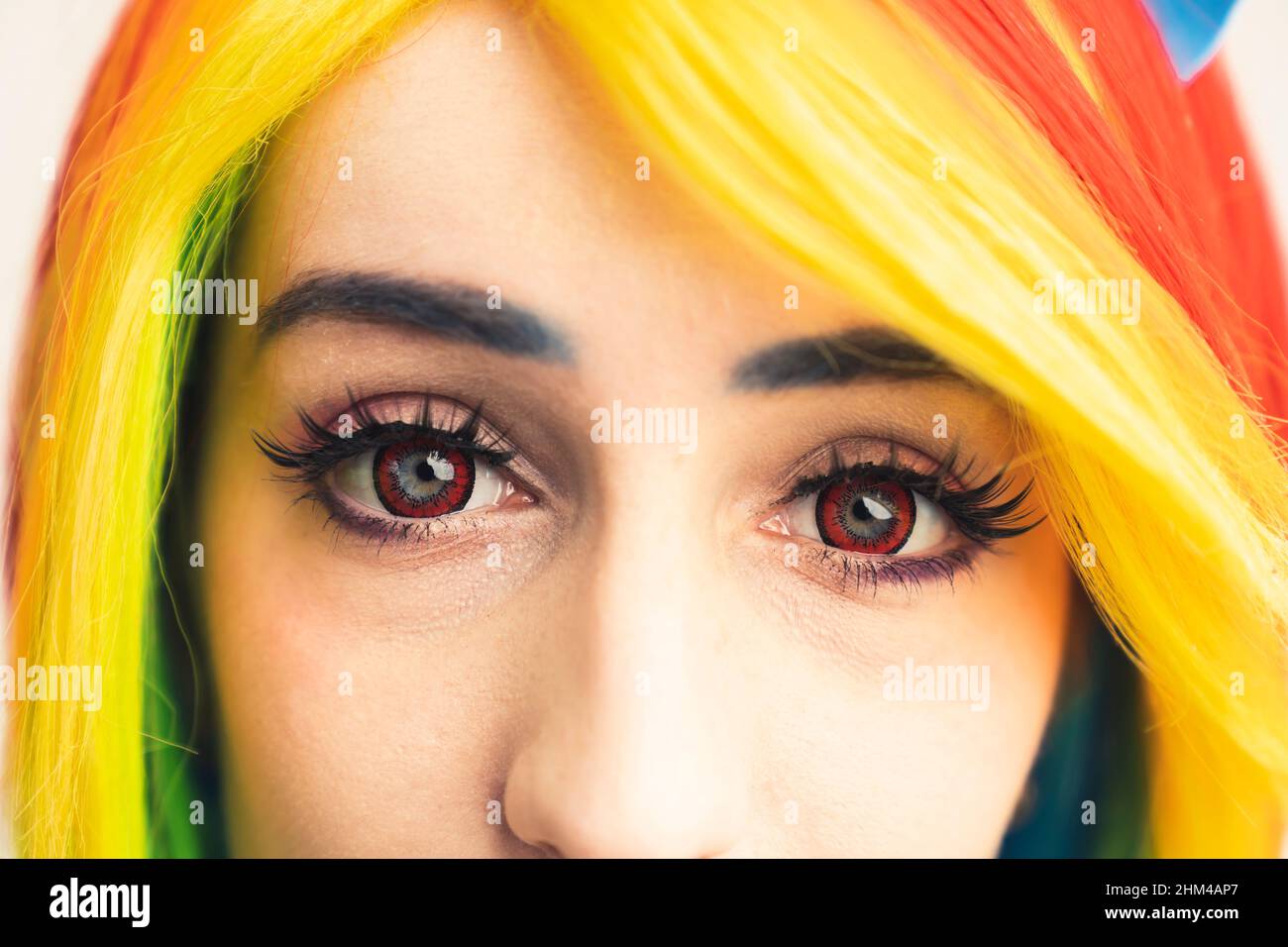 Rainbow-haired girl with red eyes and long dark lashes looking into the camera extreme close-up shot. High quality photo Stock Photo