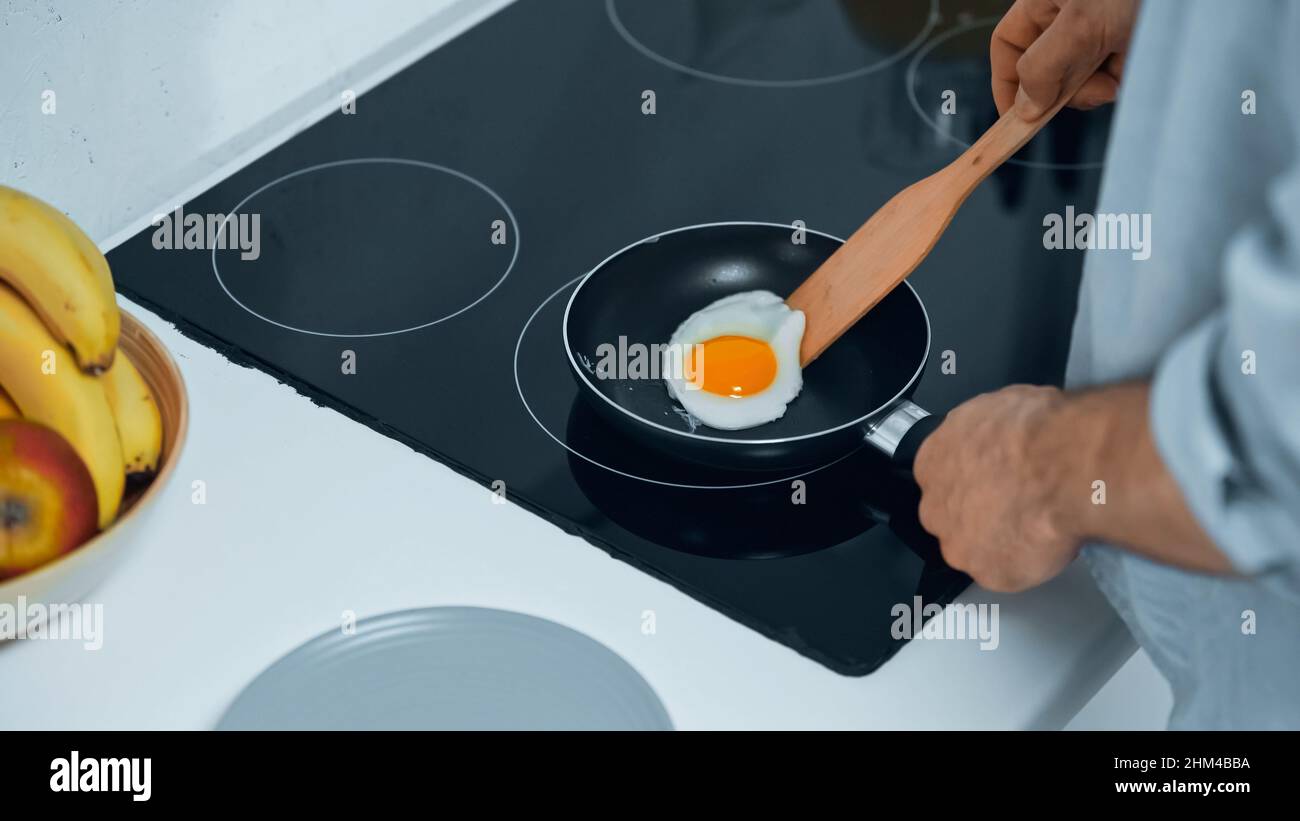partial view of man frying egg while preparing breakfast Stock Photo