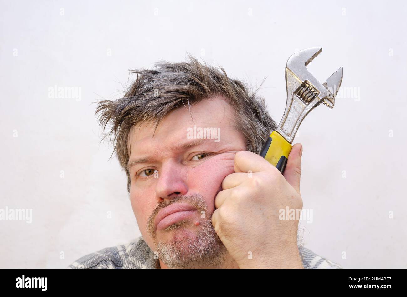 Portrait of a man with a pensive, tired face. The male supports his head with a fist and a wrench clenched in it. A man with tangled, disheveled hair Stock Photo