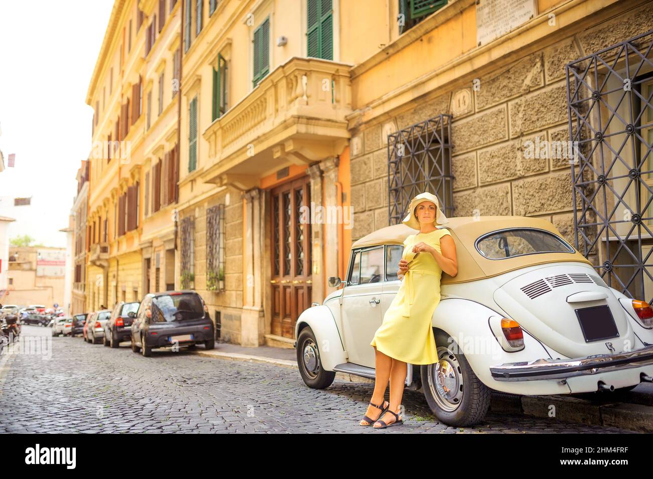 Elegant girl in a dress and hat stands near a car on a city street Stock Photo