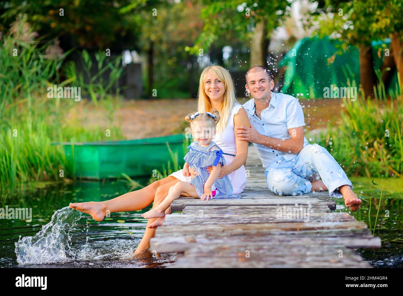 happy family resting sitting on a wooden pier, dip their feet in water and make spray, family time Stock Photo