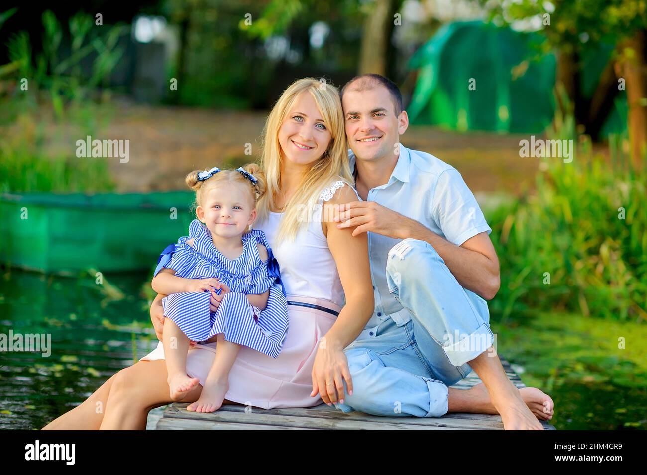 happy family resting sitting on a wooden pier, dip their feet in the water and smile, family time Stock Photo