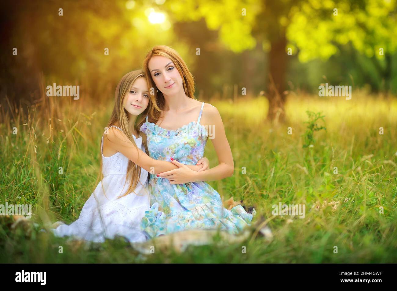 portrait of a happy mother with her daughter, sitting in the park on the grass hugging and smiling, happy motherhood Stock Photo