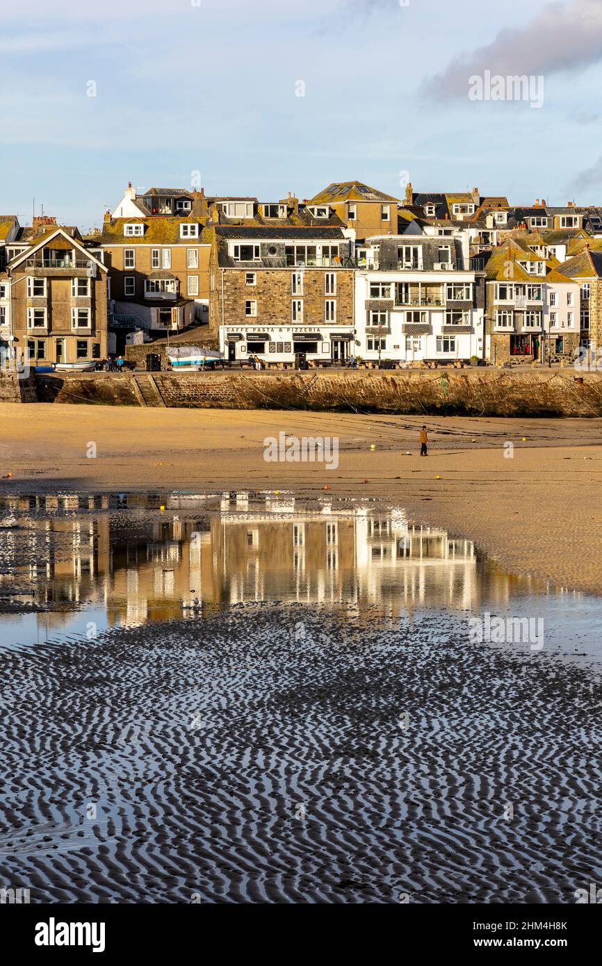 Winter sun illuminates St Ives Harbour front at low tide.  Pools in the sand reflect the buildings behind Stock Photo