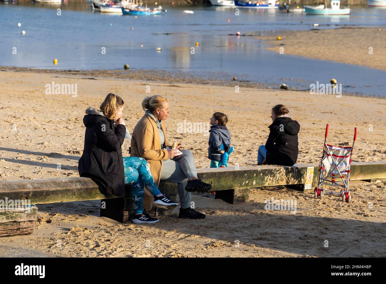 . A family sit on a slipway beam enjoying the winter sun and eating pasties Stock Photo