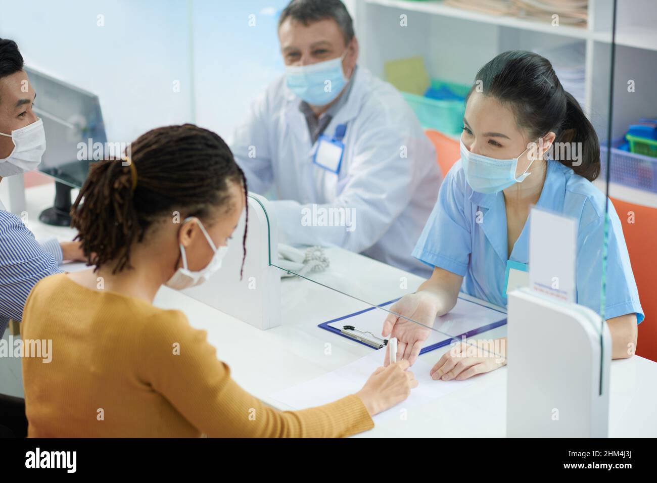 Medical nurse behind glass screen helping patient in protective mask to