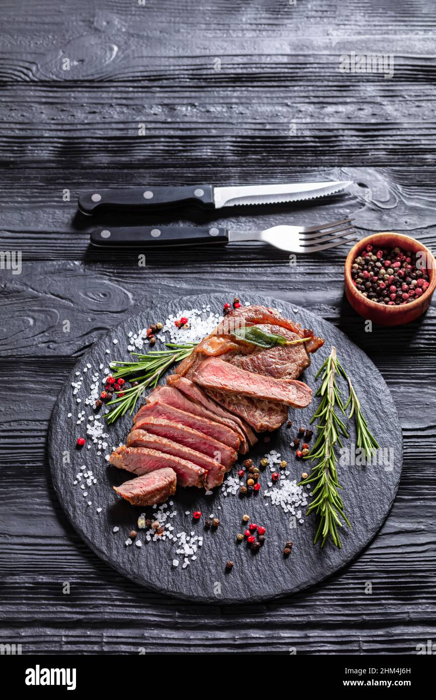 Roasted beef strip loin steak on a black slate with rosemary, salt, and