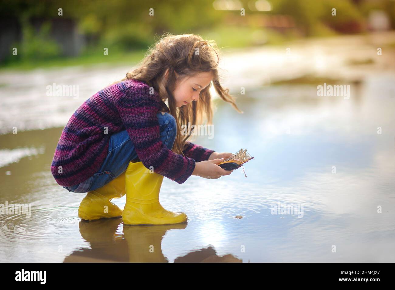 cute little girl in yellow boots plays in a puddle with a wooden boat, childhood, autumn concept Stock Photo
