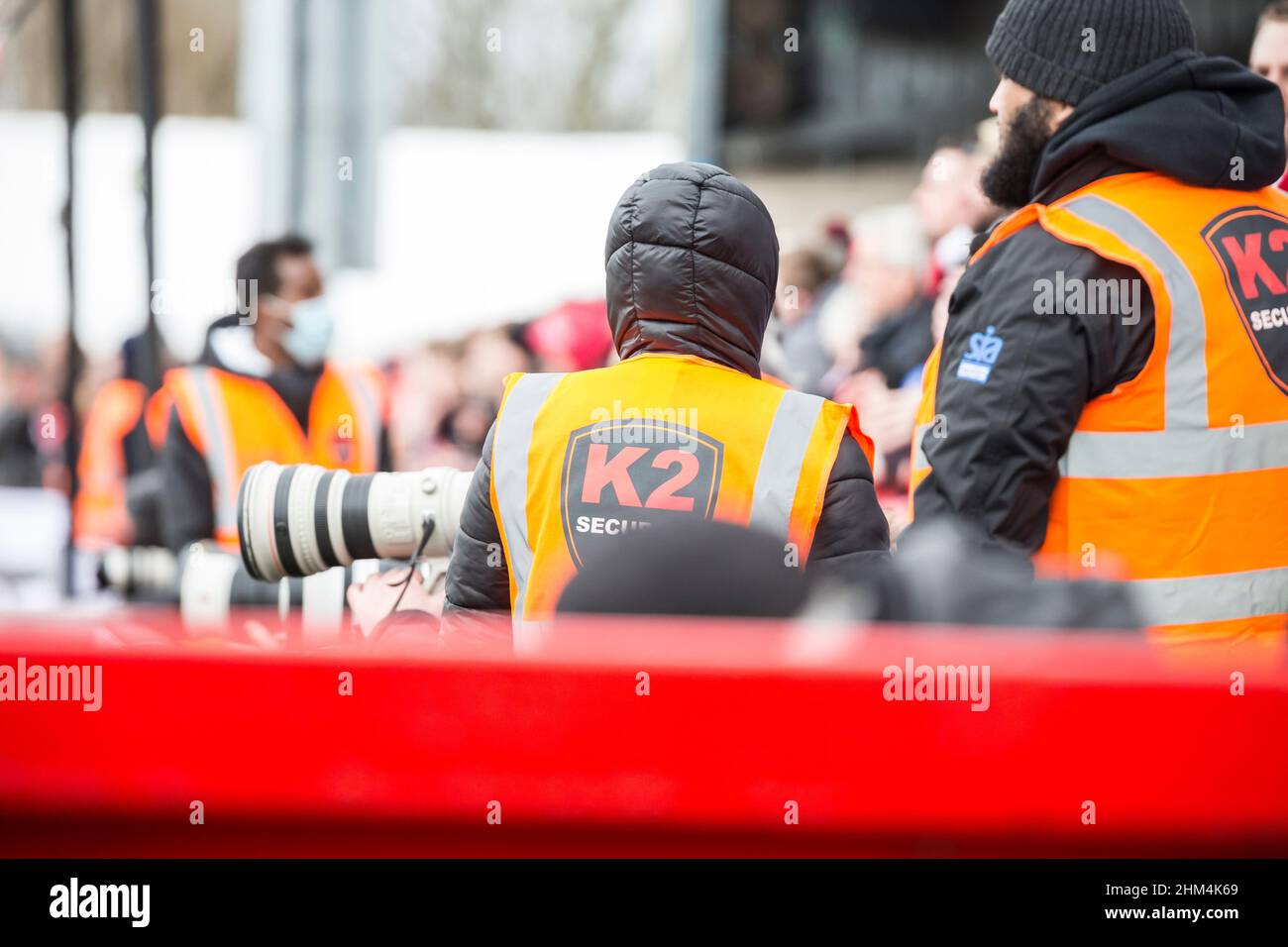 Sideline staff at UK football match: in-house security firm K2 and sports photographers using equipment with Canon prime lens. Stock Photo