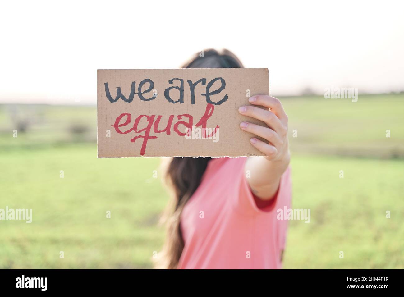 Woman holding a recycled cardboard with the inscription We are equal. Woman protesting outdoors. Concept of gender equality Stock Photo